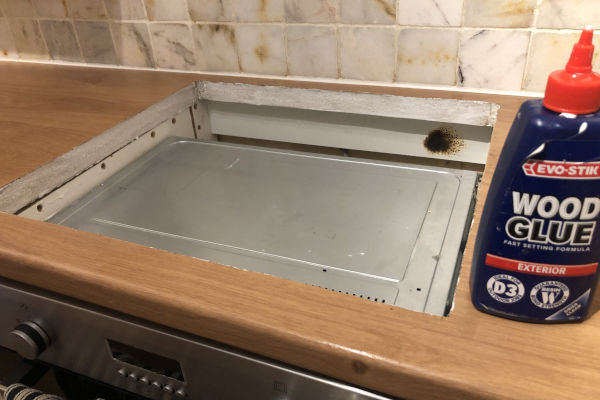 Square hole in a kitchen counter with wood glue applied to the chipboard edges