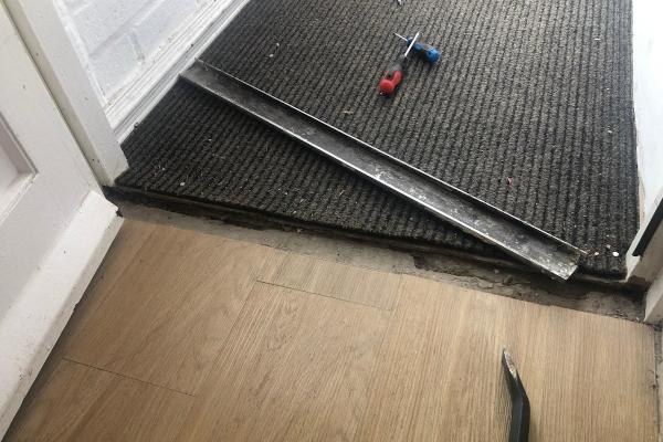 Black carpet and vinyl floor with a messy hole and a discarded metal threshold