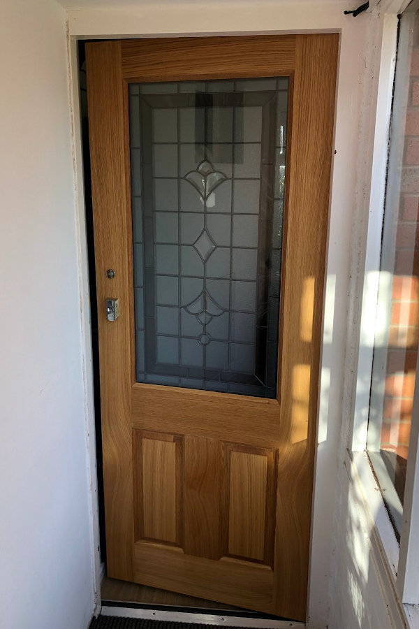 Finished front door with oak grain and shiny stainless steel metalwork