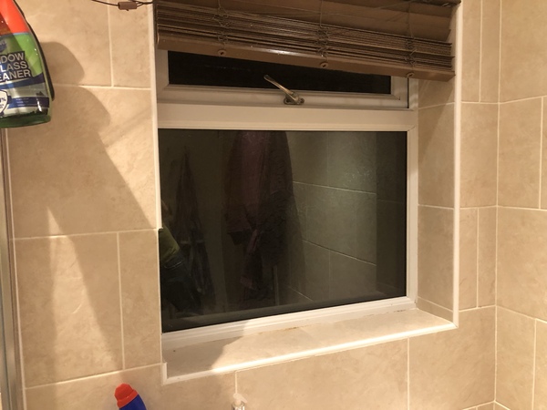 A bathroom window opening with cream porcelain tiles on the walls and reveals.