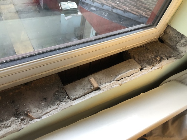 Beneath a window cill, three bricks are completely missing and replaced with a piece of wood.