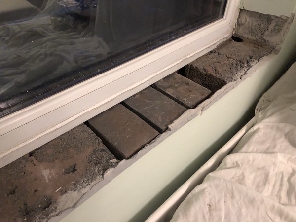 Three engineering bricks loosely placed in place of the missing bricks beneath the window cill.