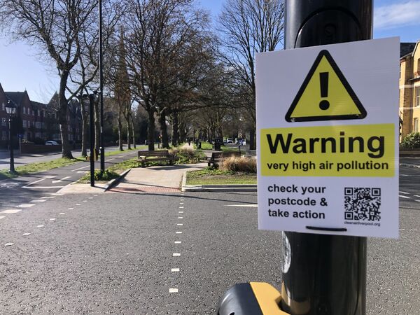 A warning sign attached to a lamp-post reading 'Warning, very high air pollution'